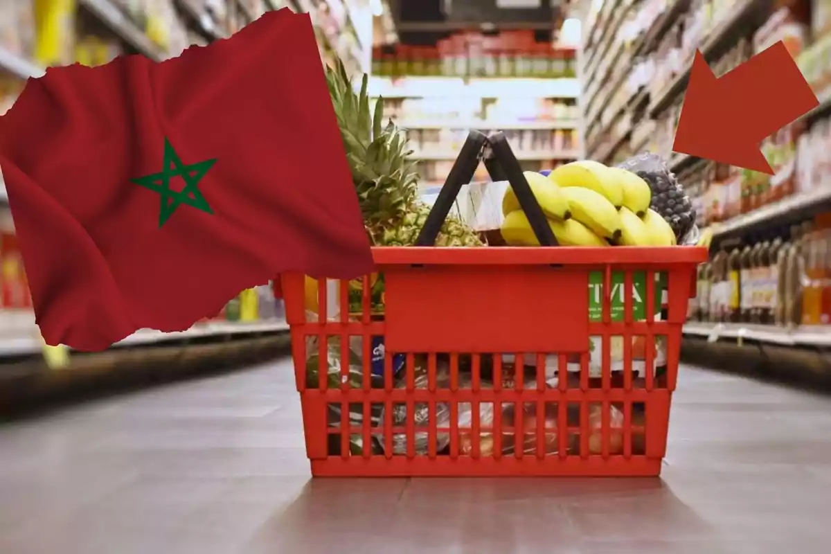 Cesta de compras roja llena de frutas y otros productos en un pasillo de supermercado, con una bandera de Marruecos y una flecha roja señalando la cesta.