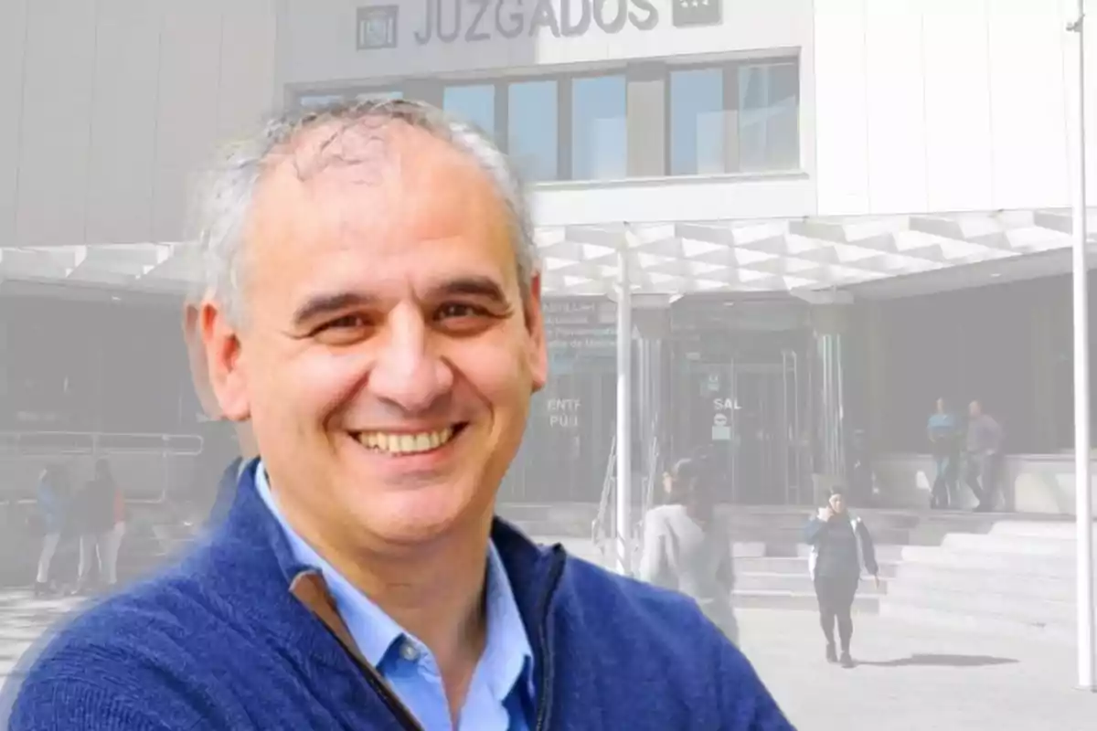 Un hombre sonriente con suéter azul frente a un edificio de juzgados.