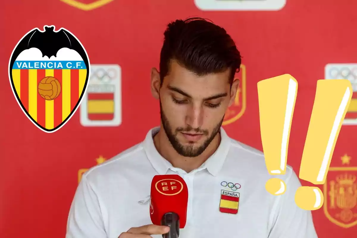 Un hombre con una camiseta blanca y un micrófono rojo de la RFEF está mirando hacia abajo, con el logo del Valencia C.F. y dos signos de exclamación amarillos sobre un fondo rojo.