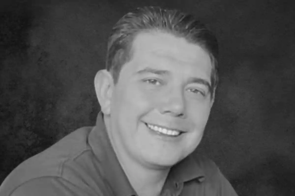 Un hombre sonriente con camisa oscura en una foto en blanco y negro.