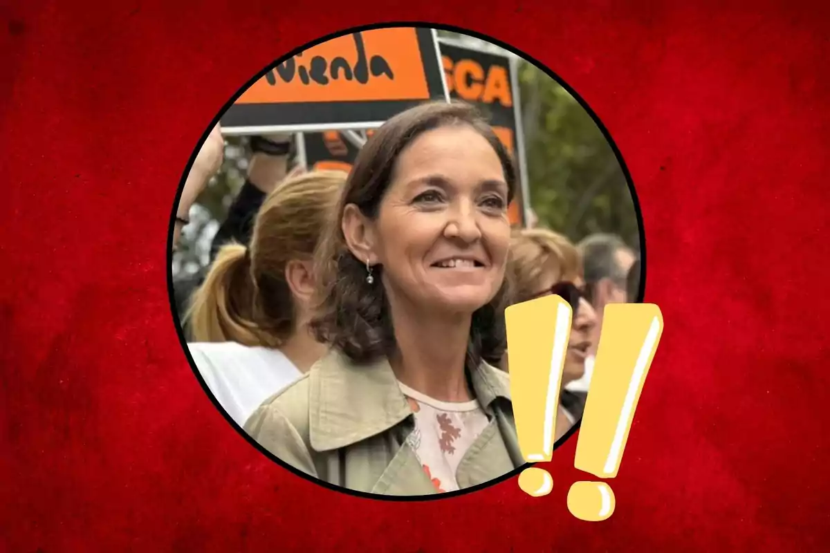 Una mujer sonriente en un evento público con un fondo rojo y signos de exclamación amarillos.