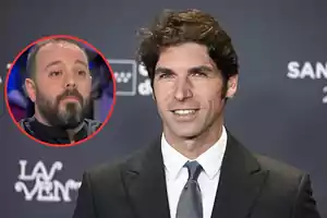 A man in a suit and tie smiles at an event while another man with a beard is shown in a red circle.