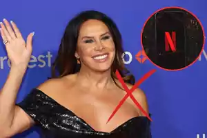 Mujer sonriendo en un evento con un vestido negro brillante y un símbolo de prohibición sobre un logo de Netflix.