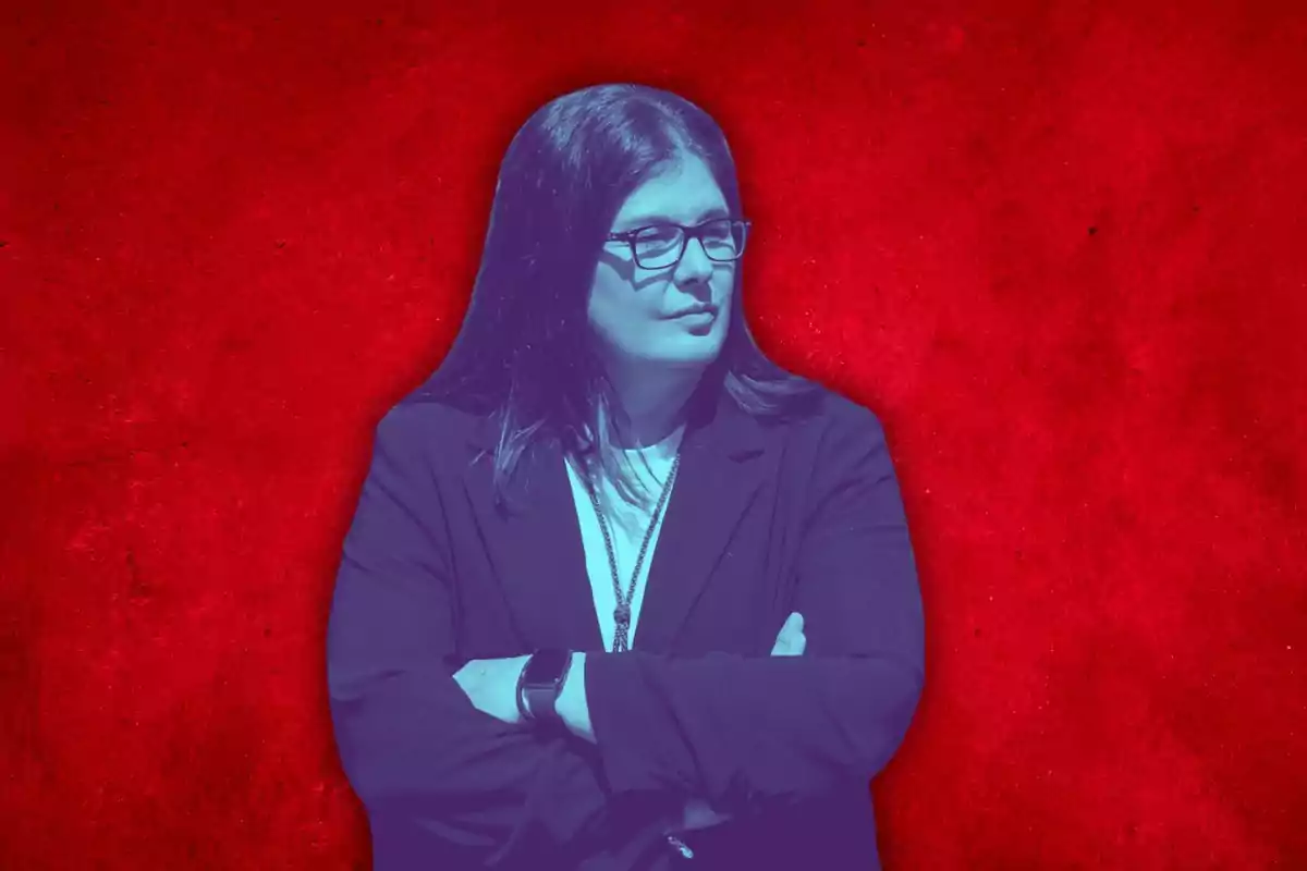 A person with glasses and a dark jacket is standing with their arms crossed against a red background.