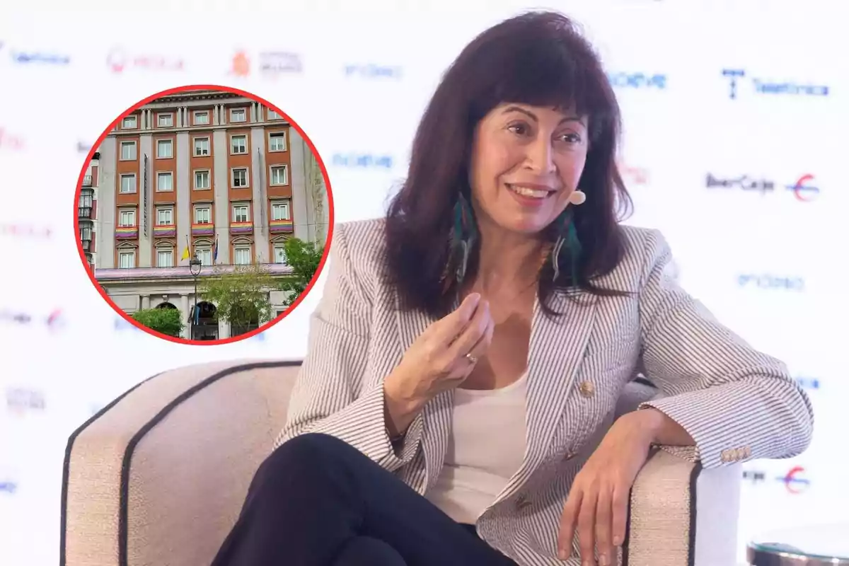 Una mujer sentada en un sillón con un micrófono en la oreja, sonriendo y gesticulando, con una imagen circular de un edificio en la esquina superior izquierda.