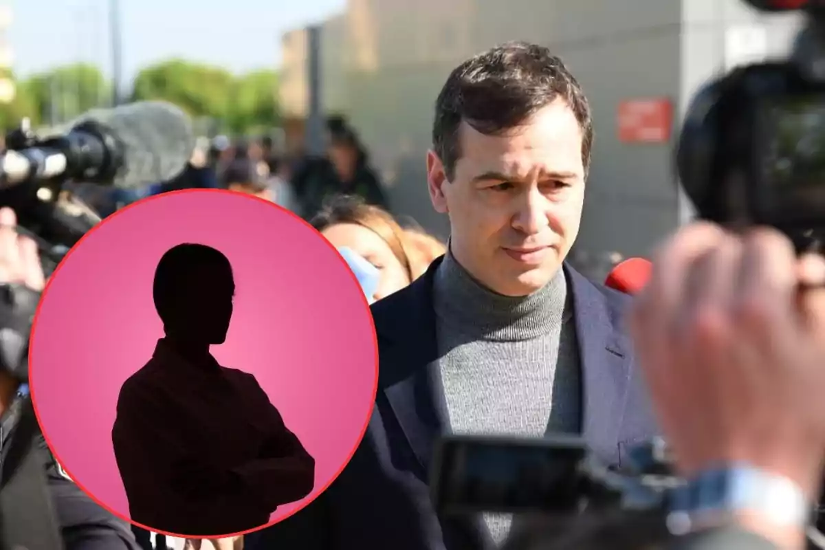 Un hombre con suéter gris y saco oscuro es rodeado por periodistas y cámaras mientras al frente aparece un círculo rosa con la silueta negra de una persona