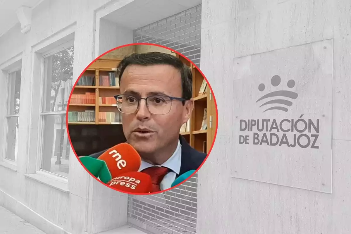 Un hombre con gafas y traje es entrevistado por varios medios frente a una estantería de libros, sobre un fondo de la fachada de la Diputación de Badajoz.