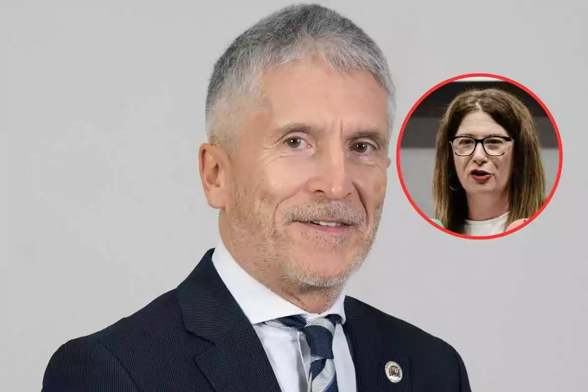 Hombre de cabello canoso con traje y corbata posando frente a un fondo claro con el retrato de una mujer con gafas en un círculo rojo en la esquina superior derecha