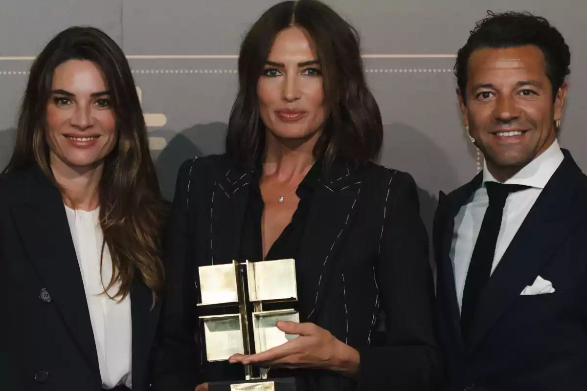 Tres personas posan juntas mientras una de ellas sostiene un trofeo.