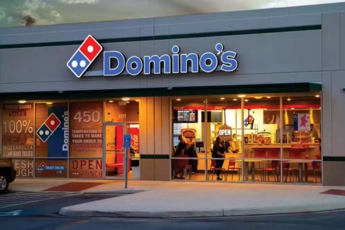 Facade of a pizzeria with the Domino's logo illuminated at dusk. Facade of a pizzeria with the Domino's logo illuminated at dusk.
