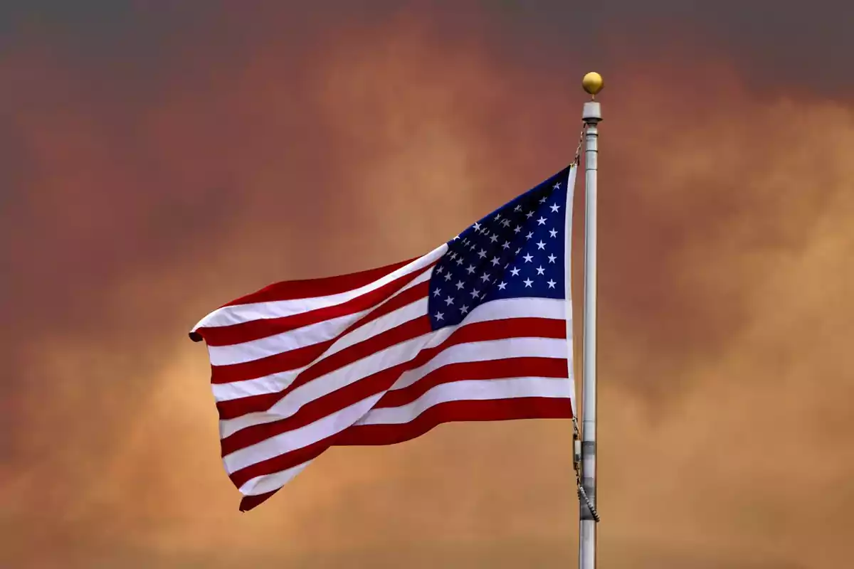 Bandera de Estados Unidos ondeando con un cielo nublado de fondo.