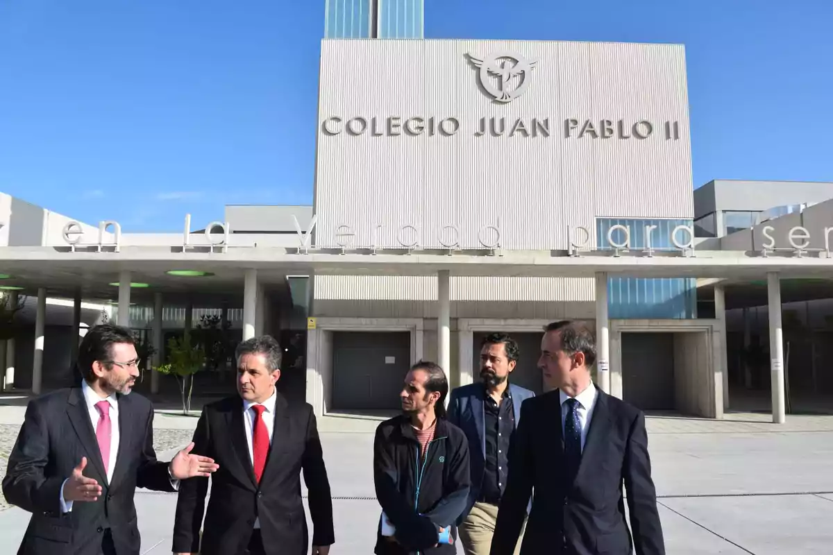 Un grupo de hombres de traje conversando frente a la entrada del Colegio Juan Pablo II.