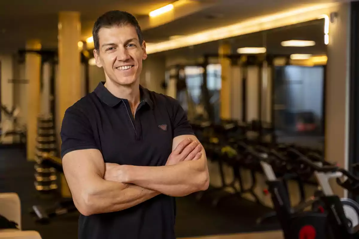 Un hombre de pie con los brazos cruzados en un gimnasio moderno.