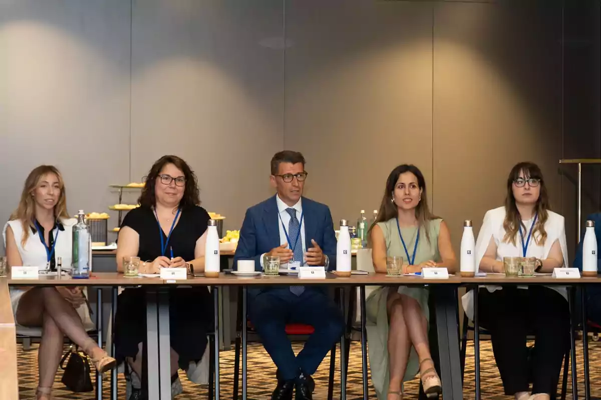 Cinco personas sentadas en una mesa de conferencia, con botellas de agua y vasos frente a ellos, en un entorno de reunión formal.