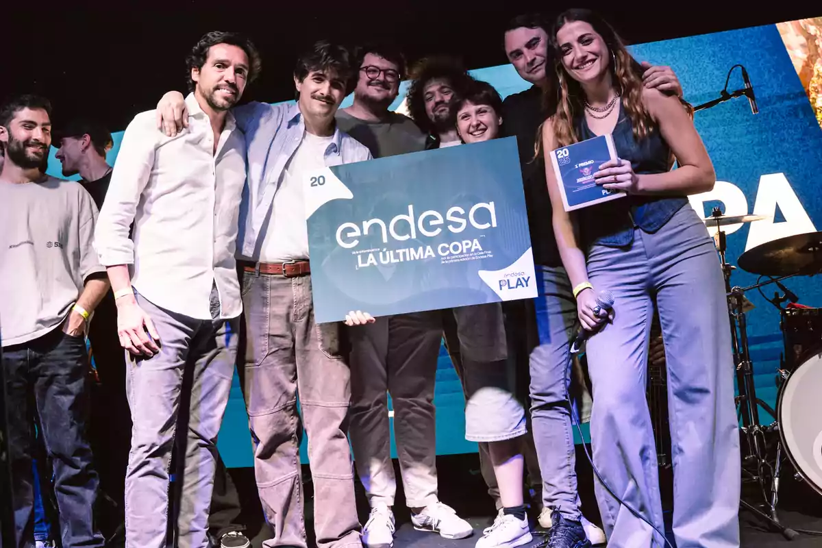 Grupo de personas sonrientes en un escenario sosteniendo un cartel grande de Endesa La Última Copa y un trofeo, celebrando un logro o premio