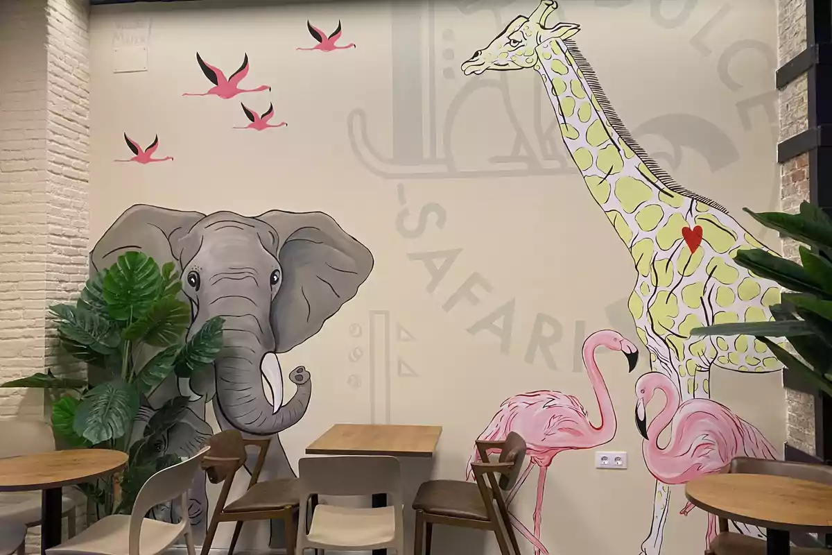 Una pared decorada con un mural de un elefante, una jirafa, flamencos y aves en vuelo, rodeada de plantas y muebles de madera en un ambiente de cafetería.