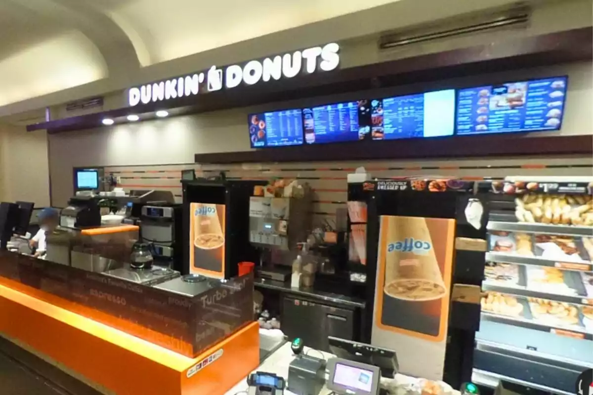 Mostrador de una cafetería Dunkin Donuts con vitrinas de donas, máquinas de café y menú digital en la parte superior Mostrador de una cafetería Dunkin Donuts con vitrinas de donas, máquinas de café y menú digital en la parte superior