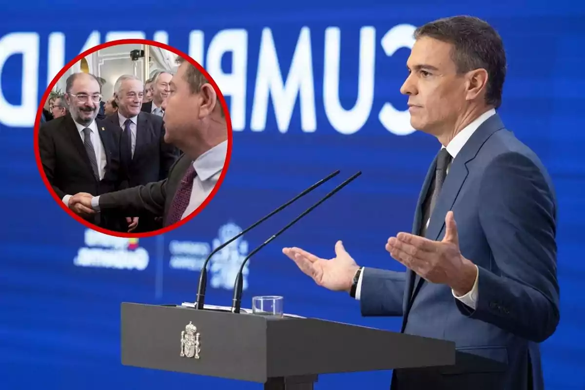 Un hombre en traje azul da un discurso en un podio con el escudo de España, mientras en un recuadro circular se muestra a varias personas estrechándose la mano y sonriendo.