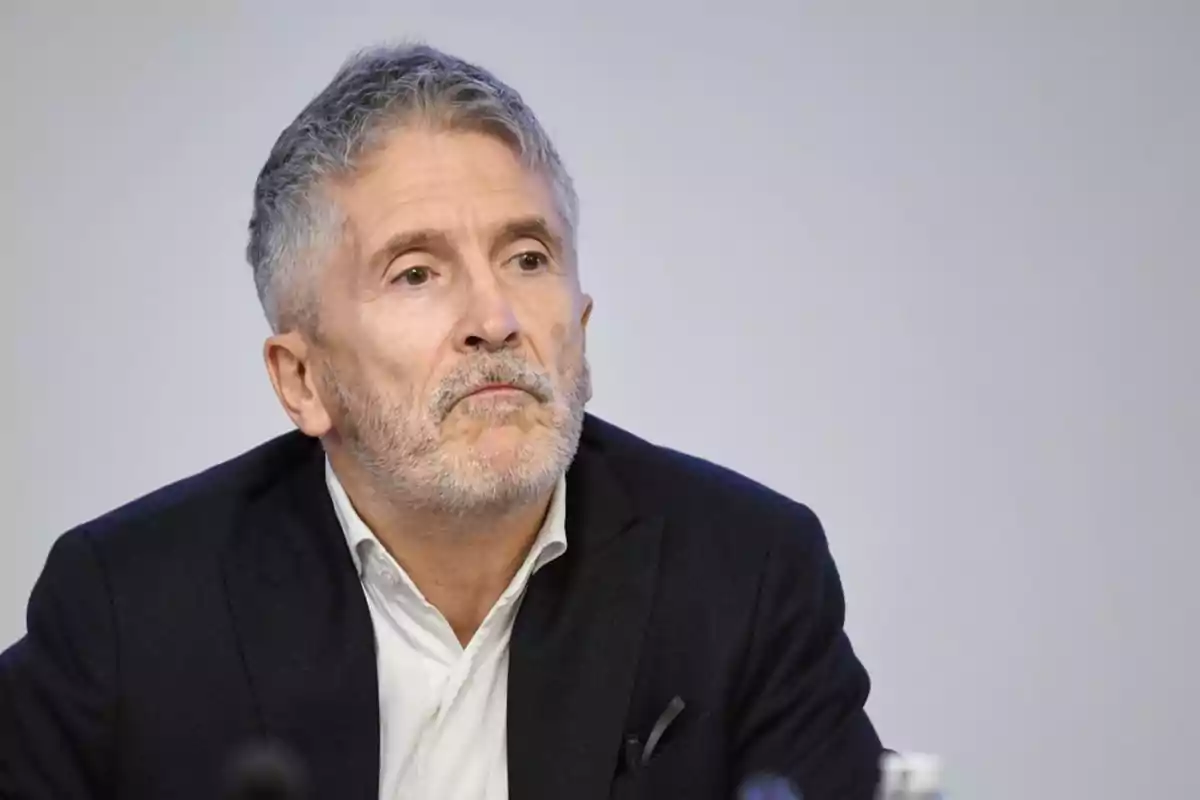 Un hombre de cabello canoso y barba corta, vestido con traje oscuro y camisa blanca, mira pensativo hacia un lado.