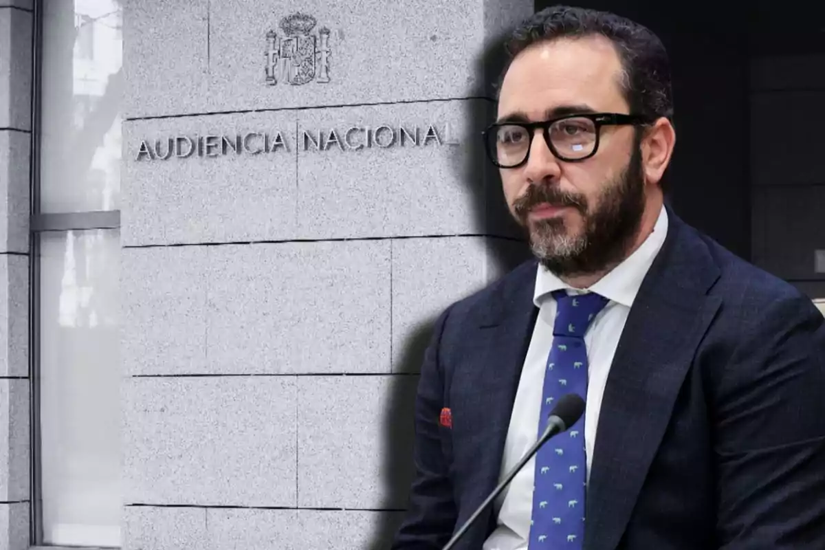 Un hombre con gafas y barba está frente a un edificio con la inscripción "Audiencia Nacional".