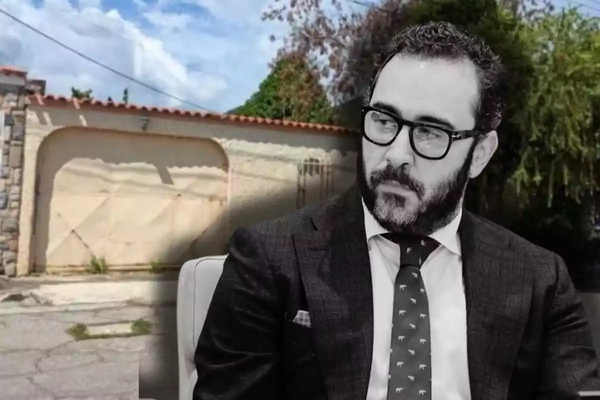 Un hombre con barba y gafas, vestido con traje y corbata, aparece en primer plano en blanco y negro, mientras que de fondo se ve una puerta de garaje y vegetación en color.