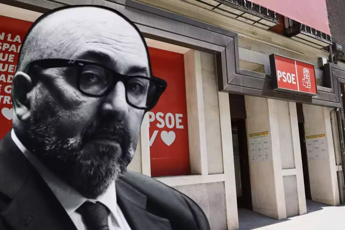 Un hombre con gafas y barba en primer plano con un edificio del PSOE de fondo.