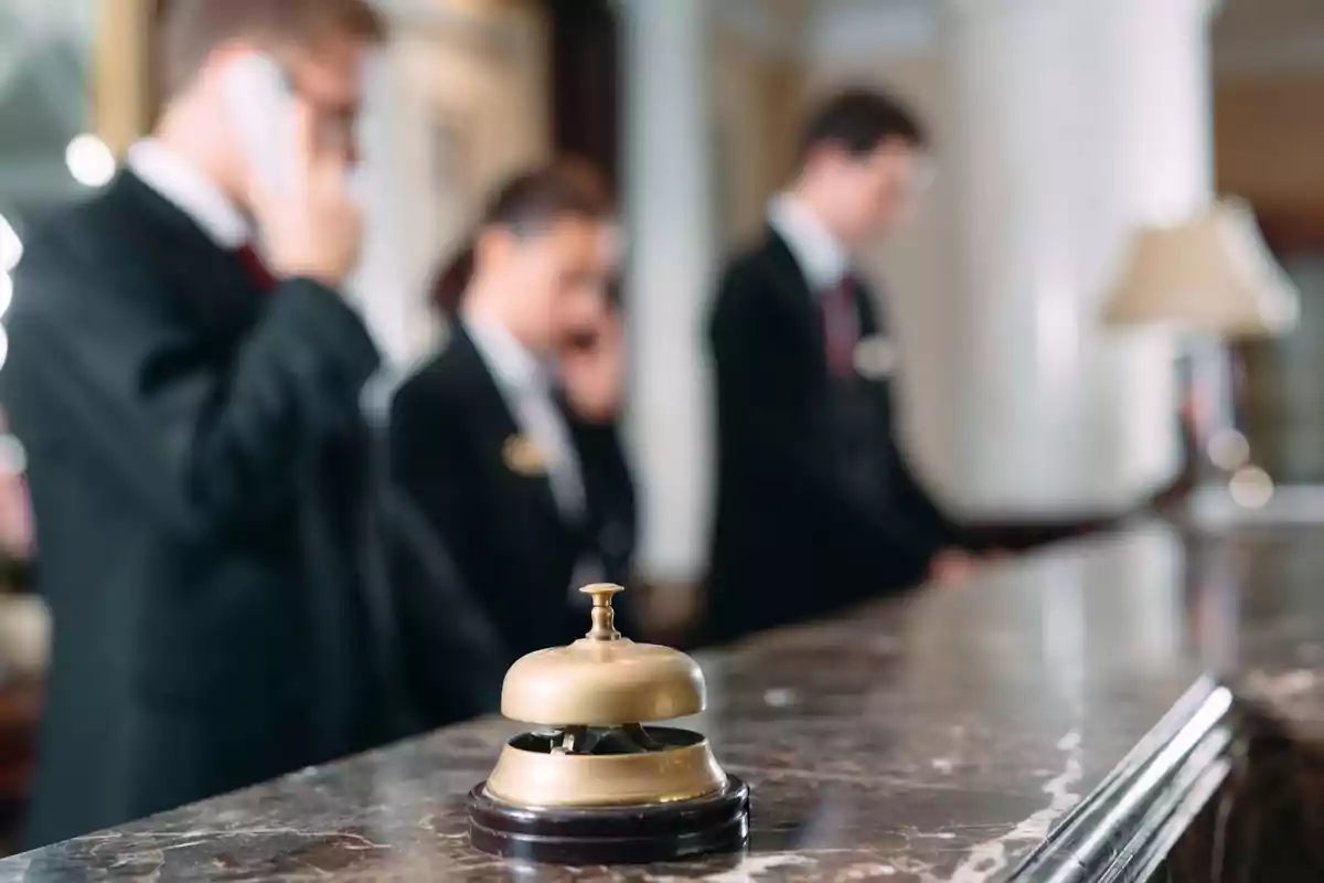 Un timbre de recepción en un mostrador de hotel con personal de fondo.