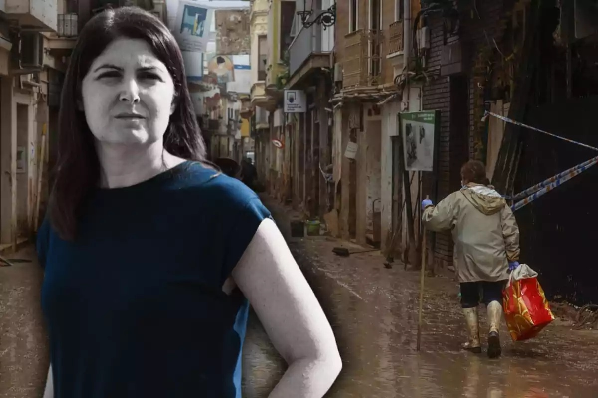 Una mujer de cabello oscuro y camiseta azul está en primer plano mientras una calle inundada y una persona con botas y un impermeable caminan al fondo.