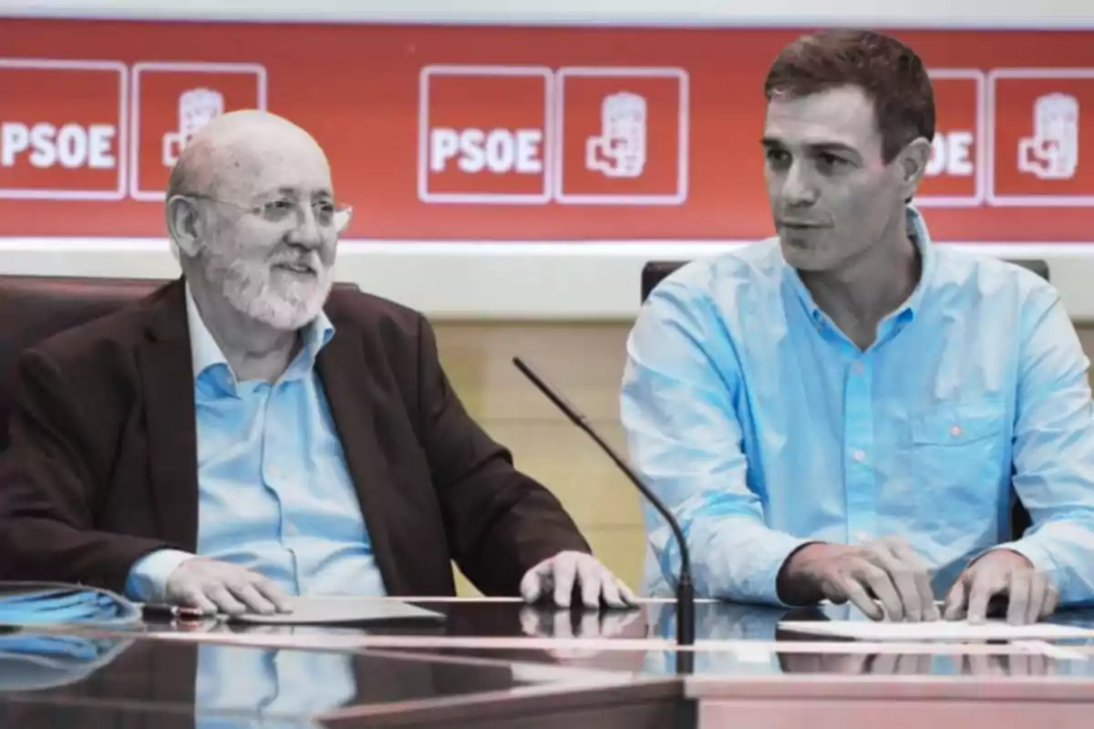 Two people sitting at a table with a background of PSOE logos.