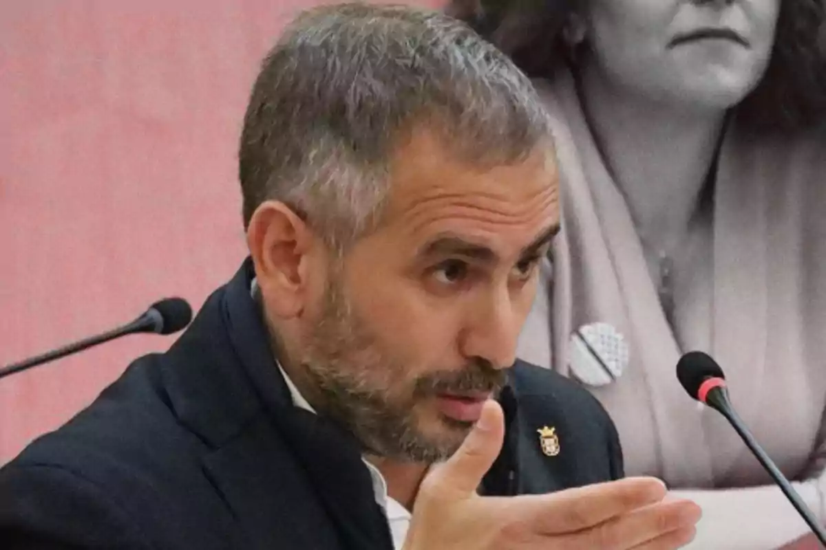 Un hombre con barba y cabello corto gesticula mientras habla en un micrófono durante una reunión.