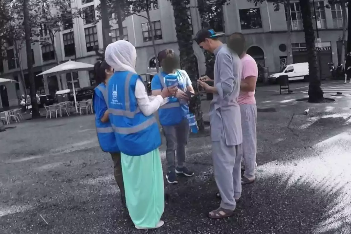 Un grupo de personas con chalecos azules interactúa en una plaza al aire libre.