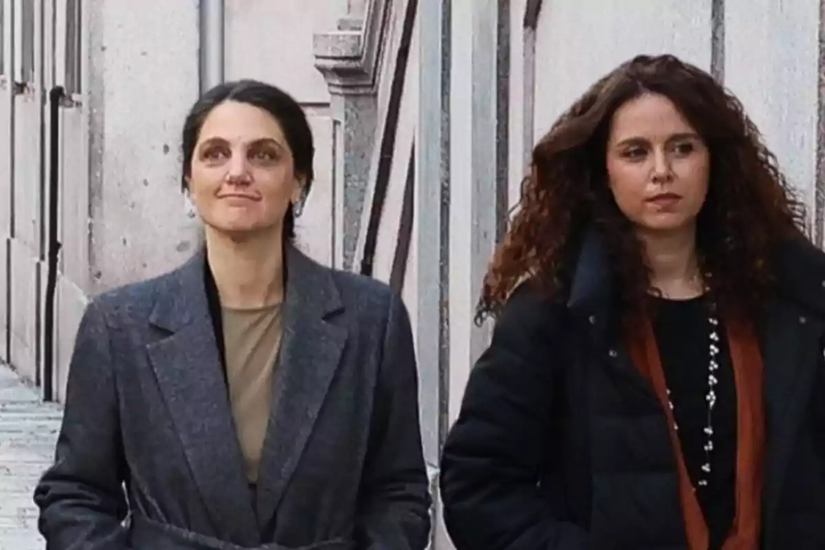 Dos mujeres caminando por una calle junto a un edificio de piedra.