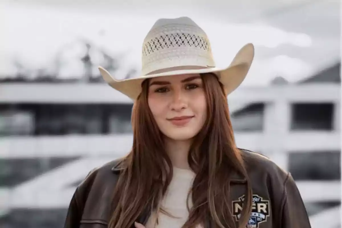 Una persona con sombrero vaquero y chaqueta de cuero sonríe suavemente frente a un fondo desenfocado.