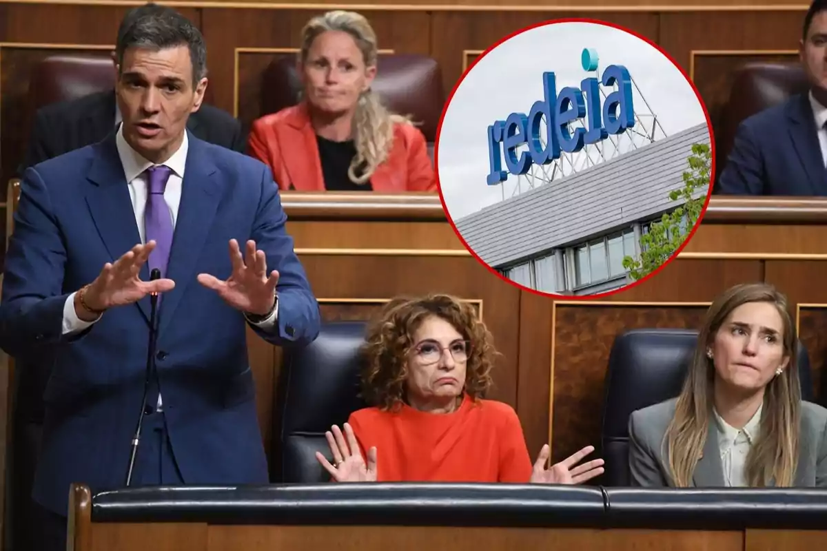 Un hombre hablando en un podio en un entorno formal con varias personas sentadas detrás de él y un recuadro que muestra un edificio con el logo de "redeia".