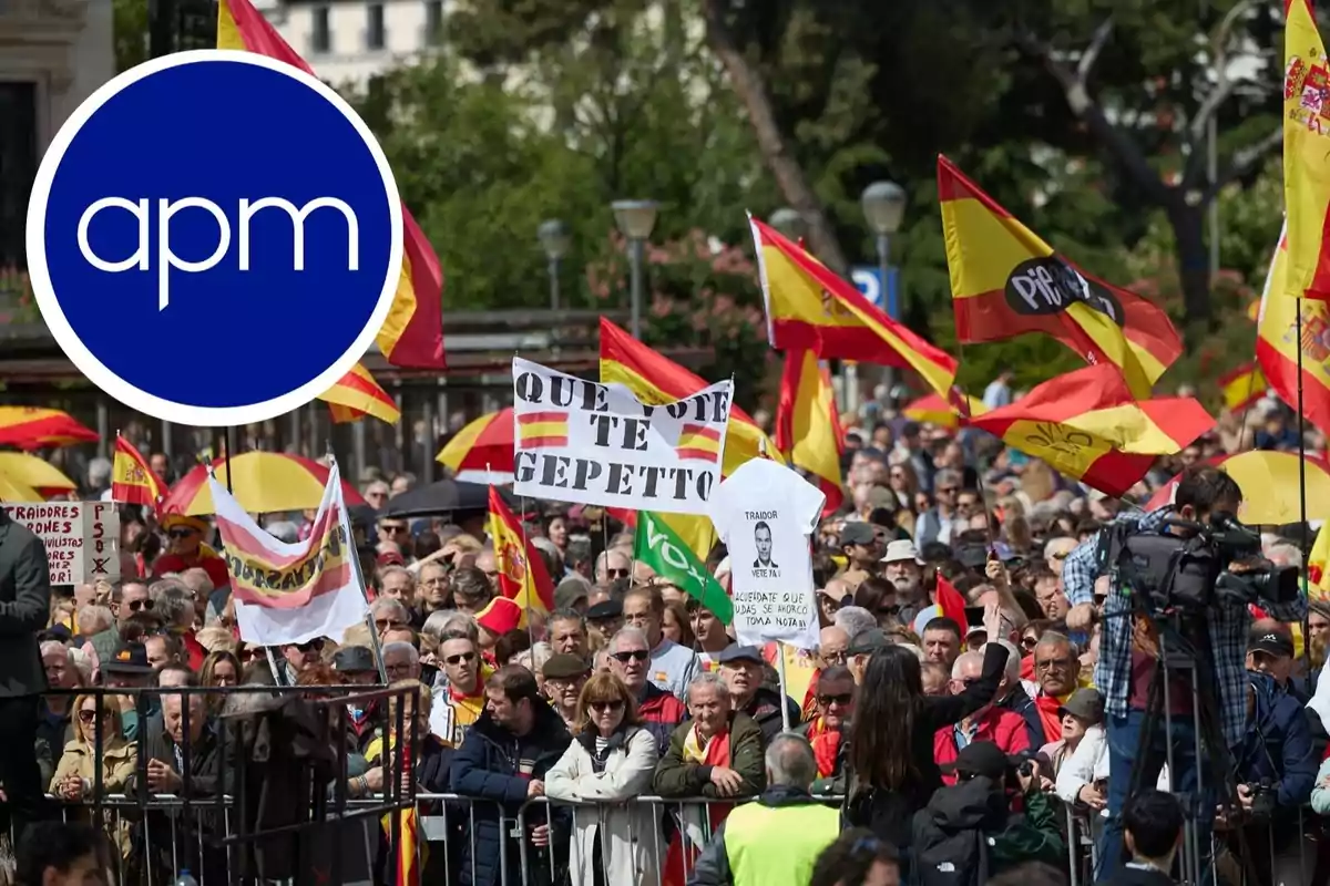 Una multitud se reúne en una manifestación con banderas de España y pancartas, mientras un equipo de cámaras documenta el evento.
