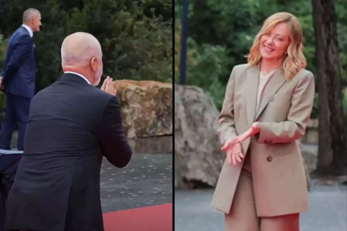 Dos personas interactúan en un evento al aire libre, una de ellas está de espaldas con las manos juntas y la otra sonríe mientras aplaude, ambas están vestidas formalmente.