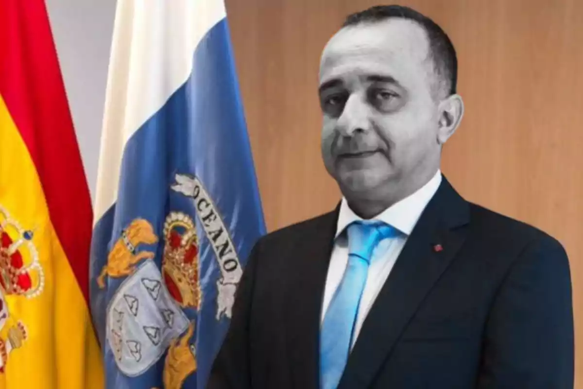 Un hombre en traje con corbata azul frente a las banderas de España y Canarias.