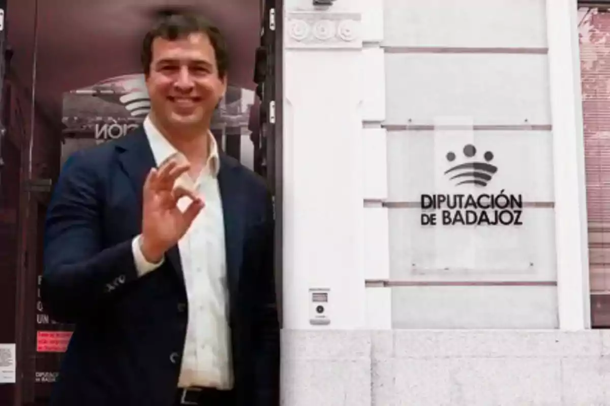 Hombre sonriente con traje oscuro haciendo un gesto de ok con la mano frente a un edificio con el letrero Diputación de Badajoz
