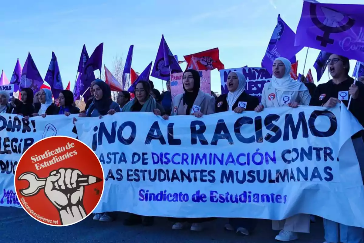 A group of people holds a banner that says "No to racism" at a demonstration, with purple and red flags in the background and a Student Union logo in the corner.