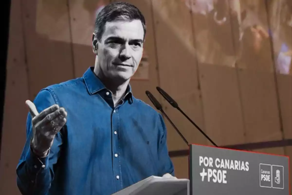 Un hombre en una camisa azul habla en un podio con un cartel que dice "Por Canarias PSOE".