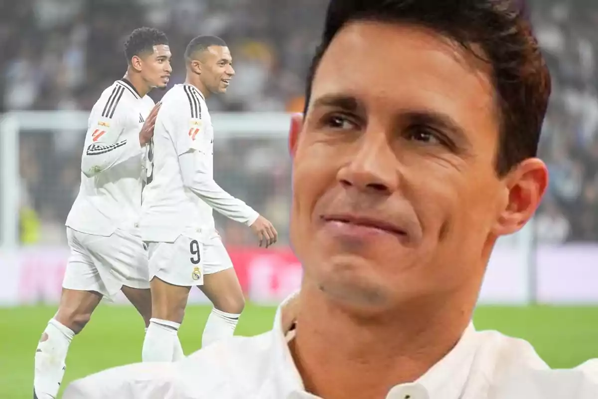 Un hombre sonriente en primer plano con dos jugadores de fútbol en el fondo durante un partido.