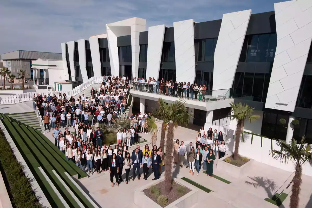 Un gran grupo de personas posando frente a un edificio moderno con palmeras y áreas verdes.