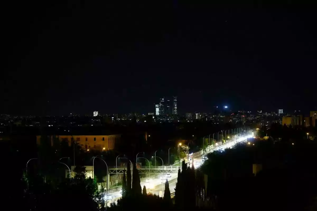 Vista nocturna de una ciudad con un horizonte iluminado y una carretera transitada en primer plano.