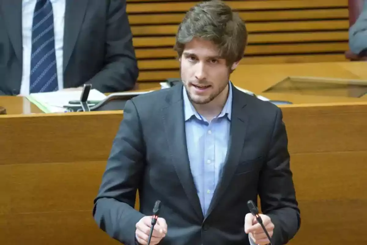 A young man speaking at a podium with microphones in a formal setting.