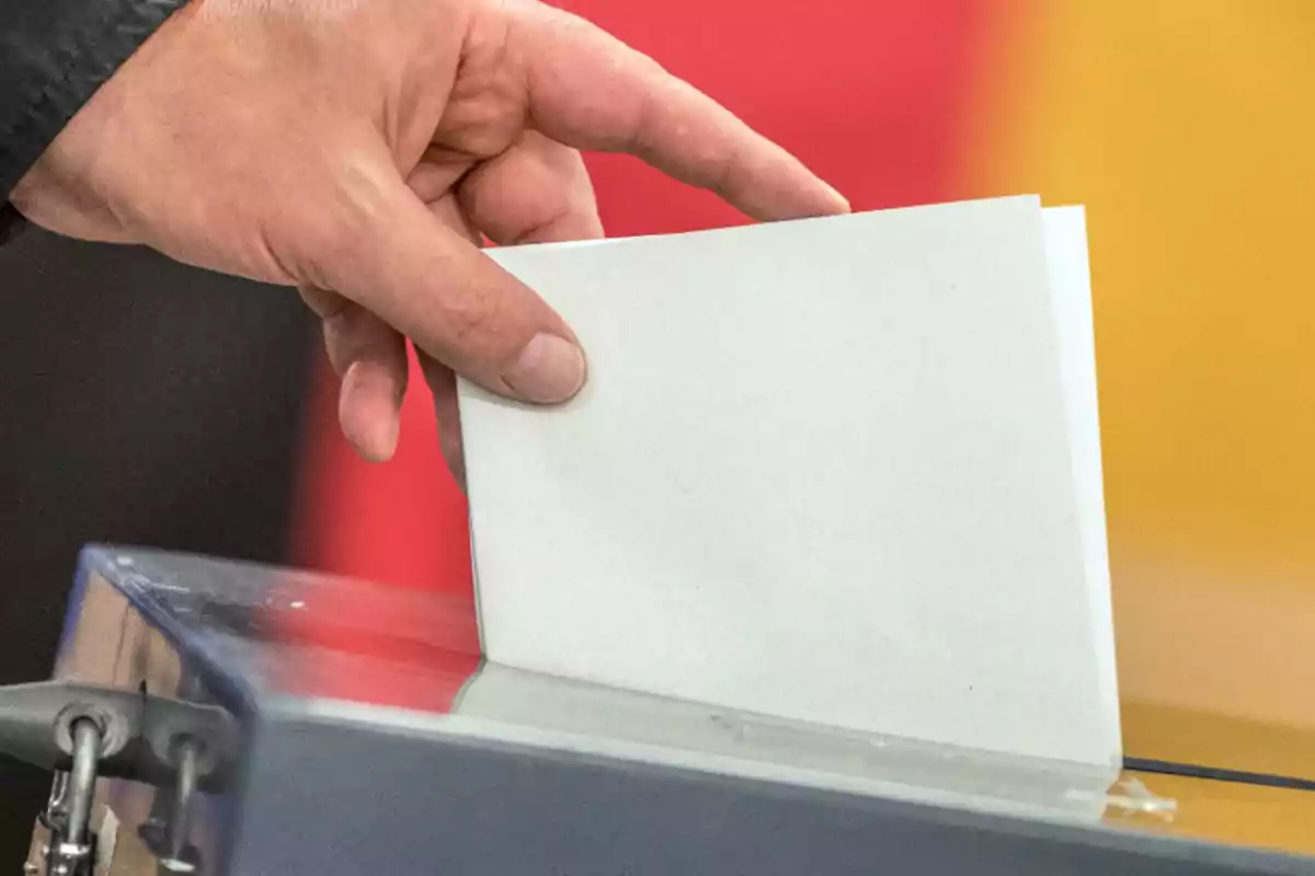 Una mano introduciendo un sobre en una urna de votación.