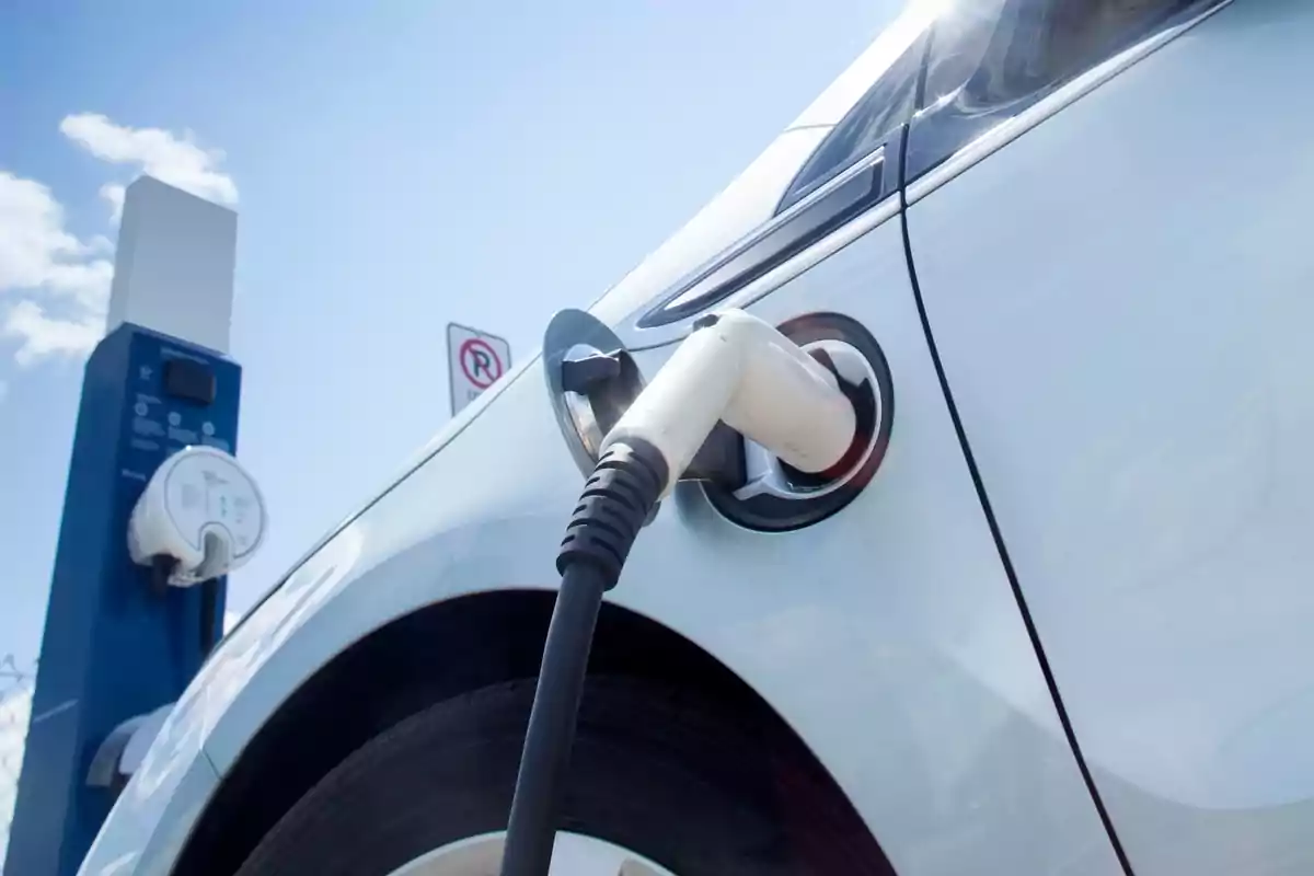 Coche eléctrico cargándose en una estación de carga bajo un cielo despejado.