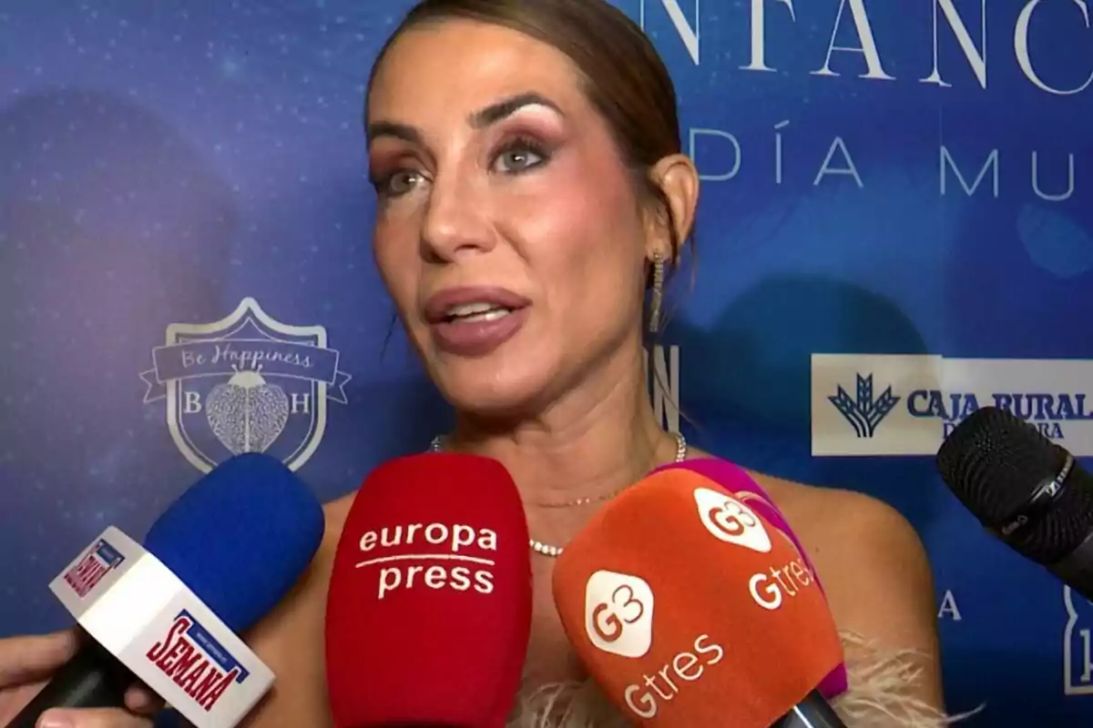 Elena Tablada siendo entrevistada por varios medios de comunicación con micrófonos de diferentes colores frente a un fondo azul con logotipos. Elena Tablada siendo entrevistada por varios medios de comunicación con micrófonos de diferentes colores frente a un fondo azul con logotipos.