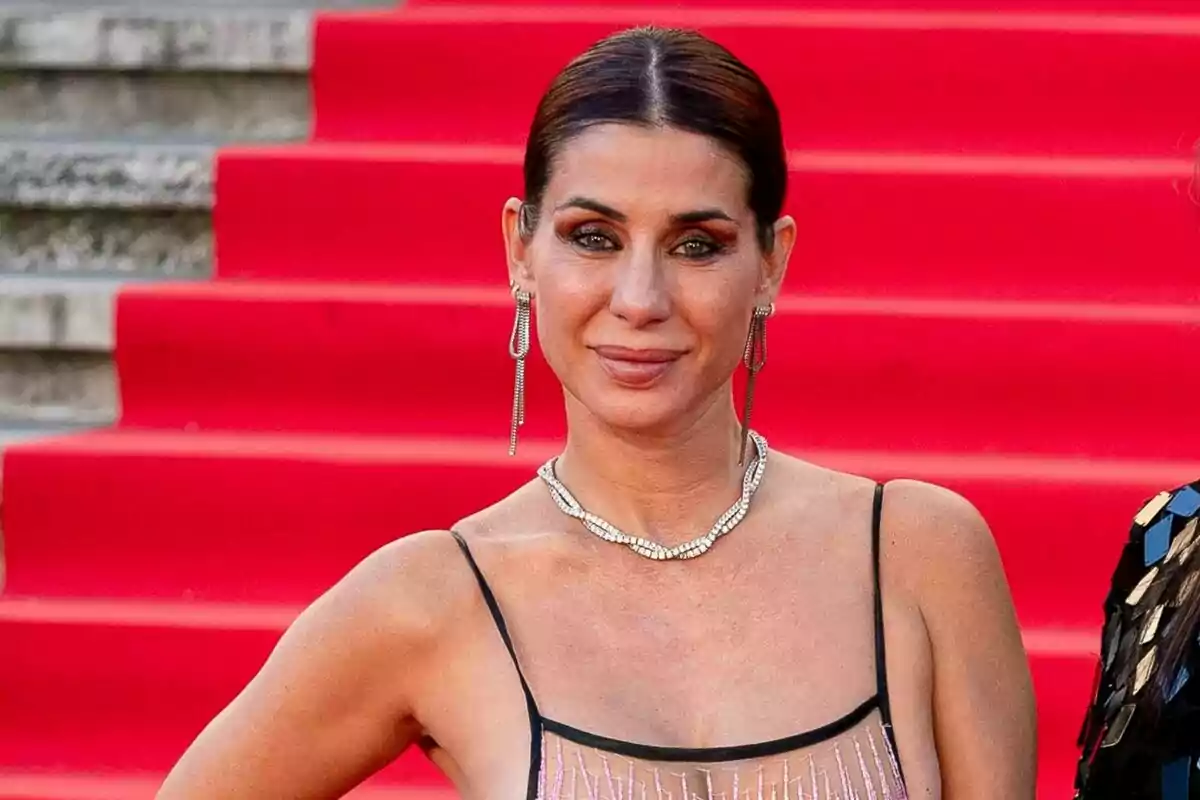 Elena Tablada con vestido elegante y joyas posando frente a una alfombra roja. Elena Tablada con vestido elegante y joyas posando frente a una alfombra roja.