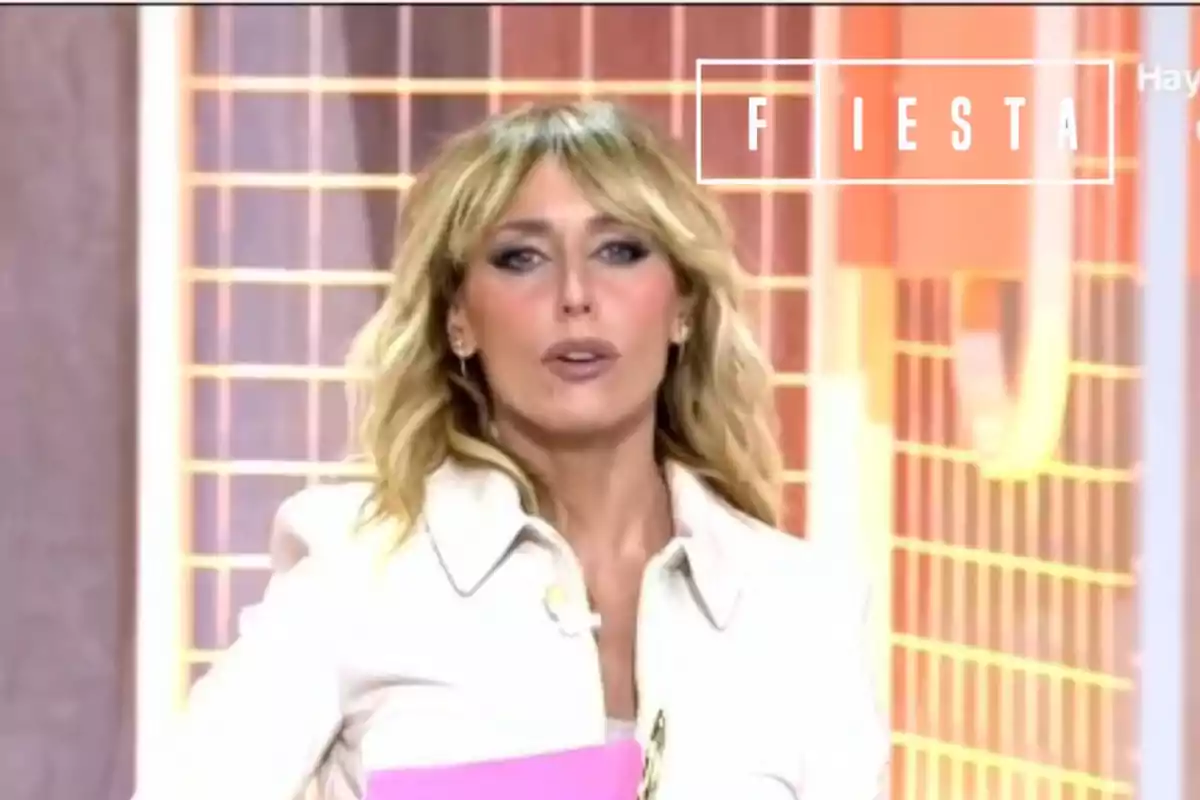 Emma García con chaqueta blanca y el pelo largo rubio, con el logo del programa 'Fiesta'