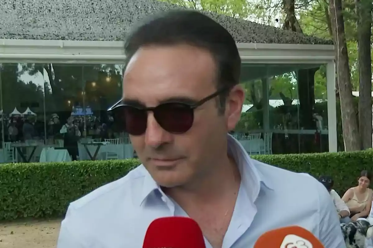 Enrique Ponce con gafas de sol y camisa clara es entrevistado al aire libre frente a un edificio con ventanas grandes. Enrique Ponce con gafas de sol y camisa clara es entrevistado al aire libre frente a un edificio con ventanas grandes.